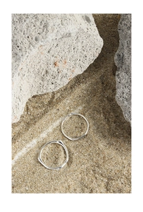 Dettaglio di due anelli in argento sterling S925 effetto metallo liquido su sabbia