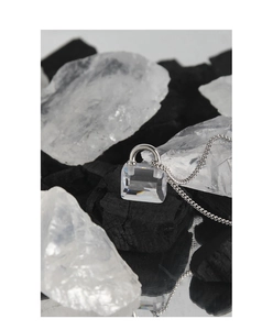 Macro shot of minimalist silver lock pendant with clear cubic zirconia on dark charcoal base