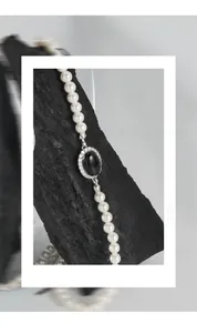 Close-up of S925 silver necklace with black agate pendant and white pearls on charred wood
