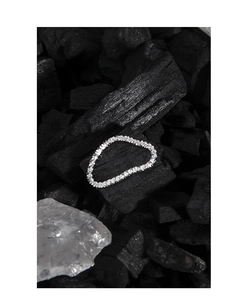 Macro detail of a shimmering silver tennis bracelet resting on charcoal with a crystal