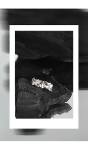 Macro detail of irregular S925 silver ring with red zircon inlay on black charcoal