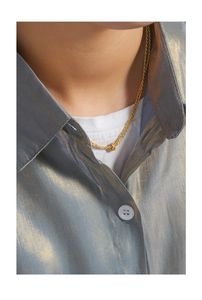Gros plan d'un collier chaîne à nœud doré porté sur une chemise en satin bleu chic