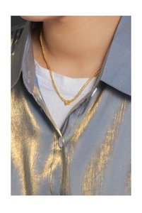 Détail d'un collier doré avec nœud tressé sur un mannequin portant une chemise en satin