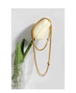 Détail d'un collier chaîne torsadée dorée enroulé autour d'un bouton de tulipe blanche