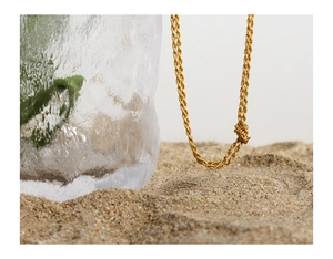 Vue détaillée du collier chaîne torsadée plaqué or 18 carats sur un décor de sable