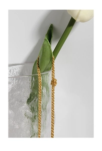Détail d'un collier chaîne torsadée dorée drapé sur un vase de fleurs blanc
