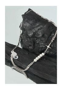Detail of S925 silver necklace with heart, cross, and pearls on textured black charcoal