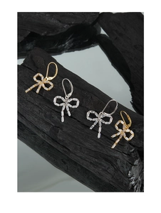 Macro detail of silver and gold bow earrings with radiant zircon crystals on charcoal