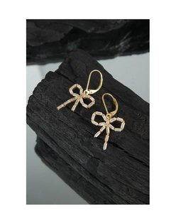 Detail of baguette-cut zircon bow earrings on a textured black charcoal base