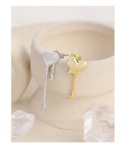 Macro shot of asymmetric liquid heart earrings in gold and silver on ceramic