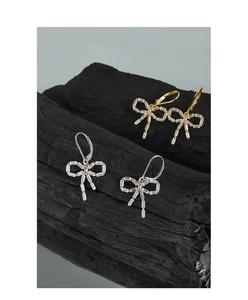 Macro detail of gold and silver bow earrings with zircon stones on charcoal background
