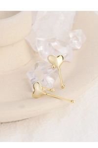 Macro shot of liquid metal heart earrings in gold finish on white ceramic display