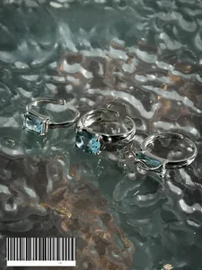 Detail of S925 sterling silver rings with blue oval zircon on a rippled glass surface