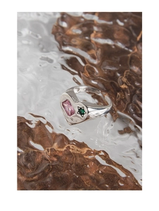 Macro shot of S925 silver heart ring with pink and green stones on textured surface