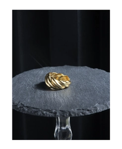 Detail view of a gold croissant ring with woven texture on a dark stone surface
