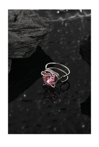 Macro shot of silver ring featuring heart-shaped pink stone and hollow band on dark stone