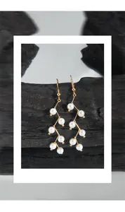 Artistic close-up of gold dangling pearl earrings displayed on textured black charcoal