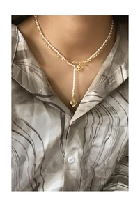 Close-up of layered heart lock pearl necklace worn over an elegant patterned shirt