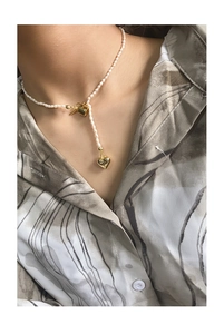 Detail view of a pearl necklace with a gold heart pendant and T-bar clasp on a model