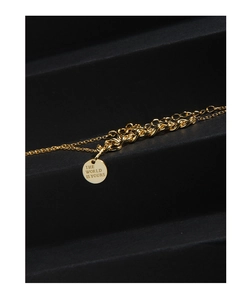 Macro detail of gold round coin necklace engraved with THE WORLD IS YOURS on black surface