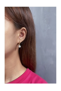Close-up of a gold disco ball drop earring with white crystals on a female model