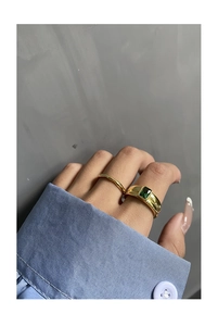 Close-up of a gold ring set with emerald cut green stone and wavy minimalist band
