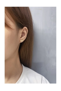 Close-up of golden curved wing stud earrings with zircon inlay on female earlobe