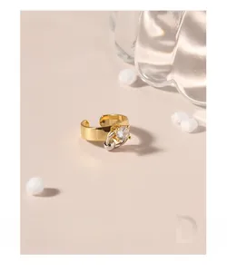 Détail d'une bague dorée en zircone avec boucle argentée sur fond rose