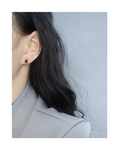 Détail des boucles d'oreilles ovales noires avec pétales dorés portées par un mannequin