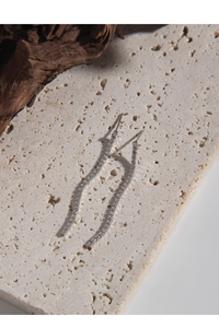 Macro detail of silver streamline earrings with micro-set zircons on beige stone base