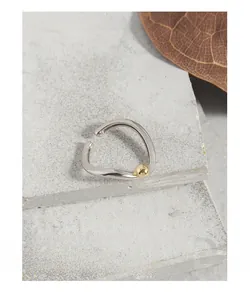 Close-up of geometric S925 silver ring with a gold bead on a textured stone surface