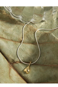 Close-up of golden heart pendant on a silver snake chain over an autumn leaf