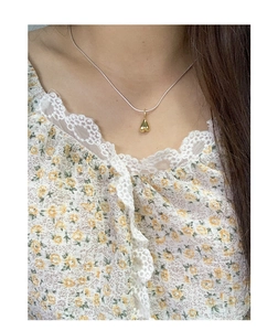 Close-up of a two-tone heart pendant necklace worn with a yellow floral lace top