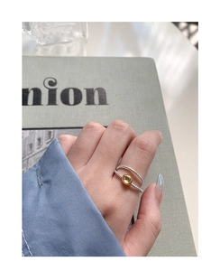 Détail d'une bague torsadée en argent avec perle dorée portée sur une main et magazine