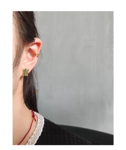 Close-up of golden geometric ear cuff and square stud with hammered texture on ear