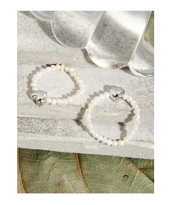 Detail of two elastic natural freshwater pearl rings with silver heart charms on stone