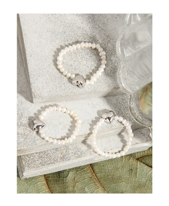 Detail shot of heart-shaped pearls rings with silver charms on grey stone steps