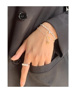 Macro shot of silver bead bracelet, gold ball pendant chain and pearl ring on black fabric