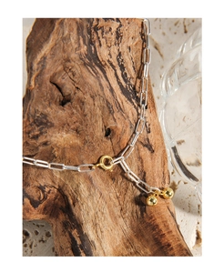 Macro detail of silver paperclip chain with gold spring ring clasp and beads on wood
