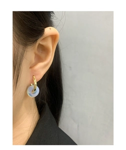 Close-up of gold geometric hoop earrings with light blue round jade bead on model