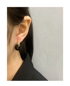 Close-up of minimalist black cylindrical drop earrings with gold metal hoops on model