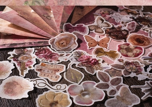 Detailed view of vintage rose and butterfly scrapbooking stickers on a dark wood background