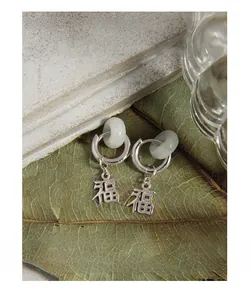 Macro detail of silver hoop earrings with green jade rings and Fu character charms