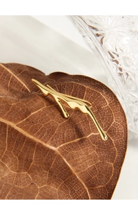 Macro shot of abstract liquid lava gold stud earrings on an autumn leaf background