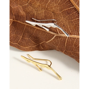 Irregular liquid lava ear cuffs in gold and silver finish on natural leaf background