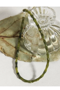 Détail du collier en jade bambou sur une feuille sèche avec un fond texturé naturel