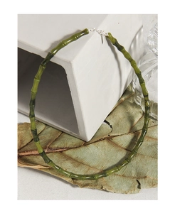 Vue détaillée du collier en bambou vert foncé sur un décor de pierres et de feuilles