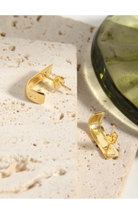 Polished gold C-shape geometric stud earrings placed on a decorative white stone