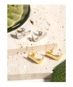 Macro shot of minimalist J-shaped curved gold and silver stud earrings on stone texture