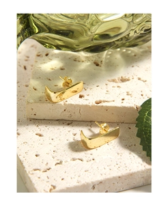 Detailed macro view of minimalist gold curved geometric stud earrings on travertine stone